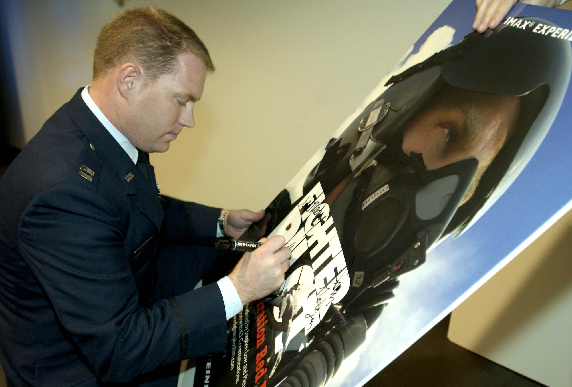 CHANTILLY, Va. -- Capt. John Stratton signs a movie poster at the premier of the new IMAX film "Fighter Pilot: Operation Red Flag."  He served as the star of the film.  The movie chronicles his experience as he participates in his first Red Flag exercise.  The film made its premier Dec. 2 at the National Air and Space Museum here.  (U.S. Air Force photo by Master Sgt. James Varhegyi) 