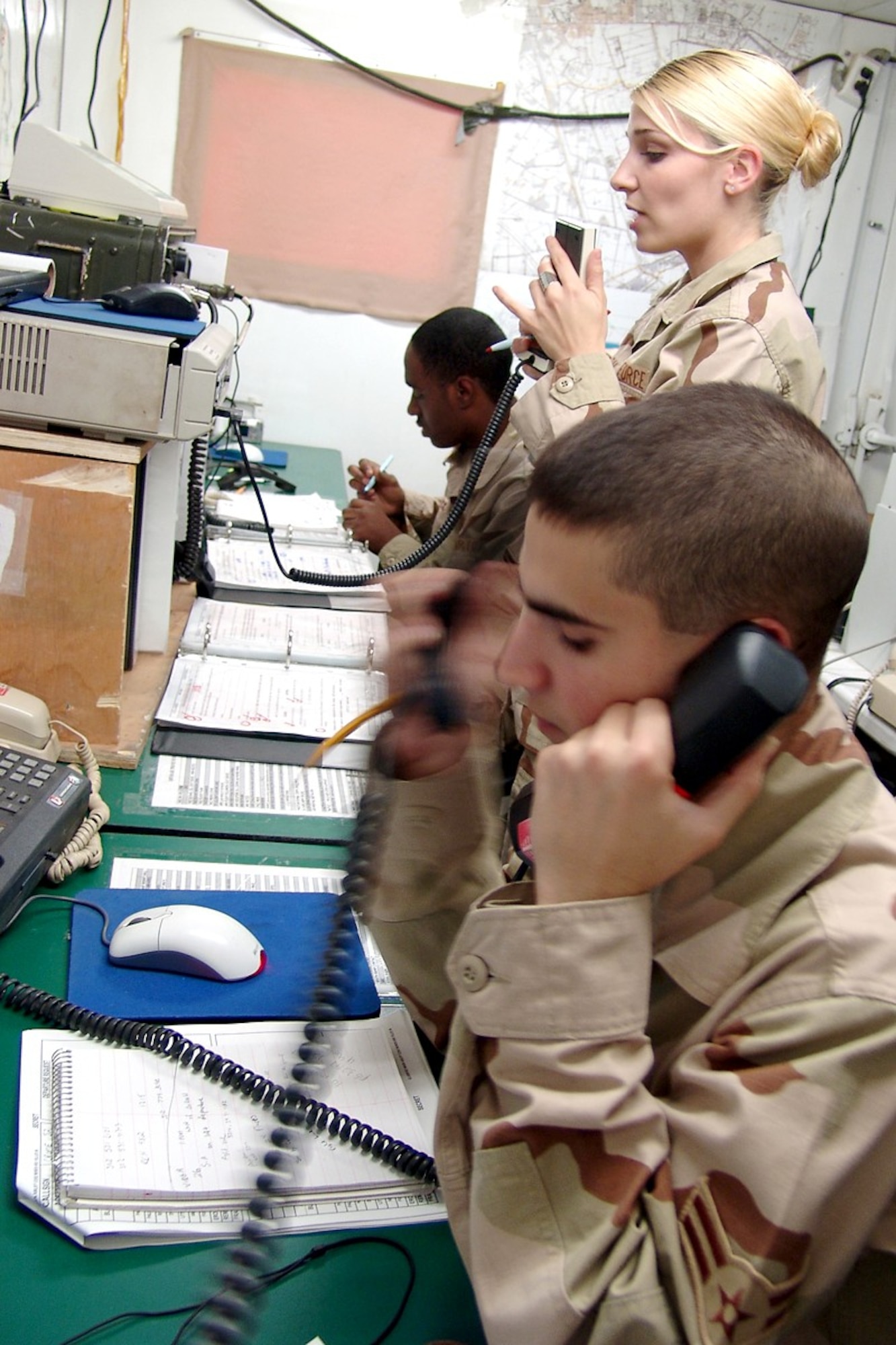 BAGHDAD, Iraq -- Airmen 1st Class Calvin Jackson (rear) and Anthony De Maio team-up in the Camp Sather command post here to handle aircraft in their area of responsibility while Senior Airman Amber Hough makes a notification to camp using the giant voice system.  Airman Jackson is deployed from Eielson Air Force Base, Alaska, Airman De Maio is from Misawa Air Base, Japan, and Airman Hough is from Yokota AB, Japan.   (U.S. Air Force Photo by Tech. Sgt. Michael O'Connor)
