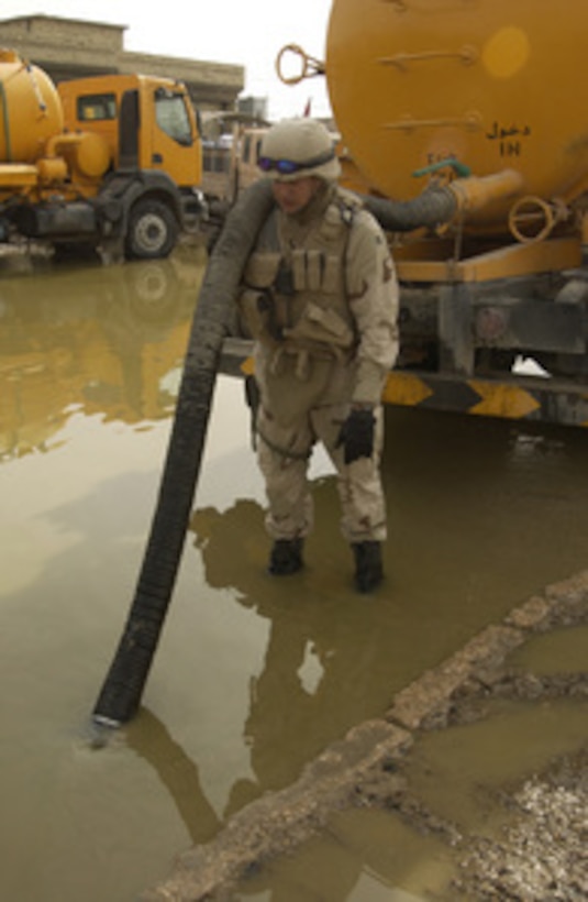 Navy Seabee Petty Officer 2nd class Langdon holds a suction hose steady as a septic tanker sucks up water from a severely flooded section of Fallujah, Iraq, on Dec. 6, 2004. Langdon is a U.S. Navy equipment operator from Naval Mobile Construction Battalion 23 from Ft. Belvoir, Va. The Seabees are working on several cleanup and reconstruction projects throughout the city to prepare the area for residents to return. 