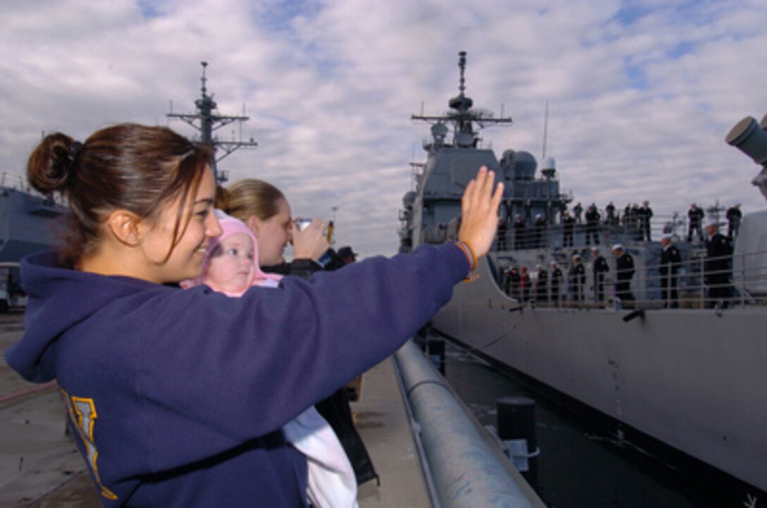 Veronica Rand (left), Theresa Trowbridge (right), and goddaughter Kyrsten Trowbridge wave good-bye from the pier at Naval Station San Diego, Calif., as they watch their loved one Petty Officer 3rd class Tom Rand aboard the USS Bunker Hill (CG 52) put out to sea on Dec. 6, 2004. Rand is a Navy fire controlman. 