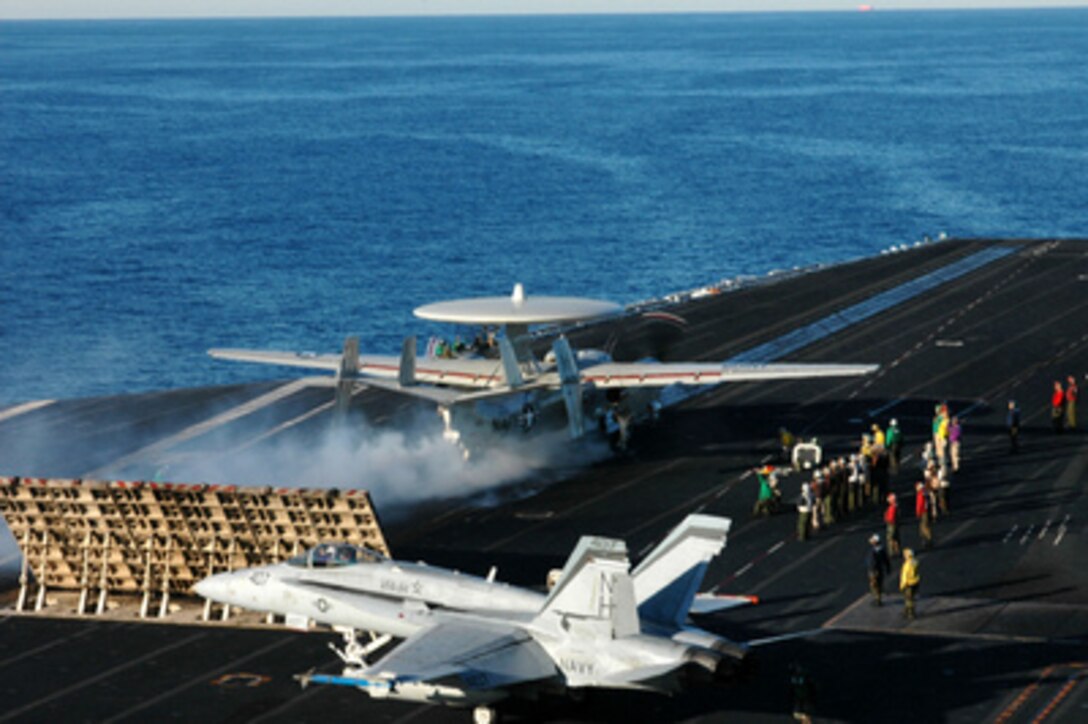 An E-2C Hawkeye launches from one of four steam-powered catapults as an F/A-18 Hornet taxis into position on the busy flight deck of the USS Nimitz (CVN 68) operating in the Pacific Ocean on Dec. 2, 2004. The Nimitz is conducting a Composite Training Unit Exercise off the coast of southern California. The Hawkeye is assigned to Carrier Airborne Early Warning Squadron 117. 