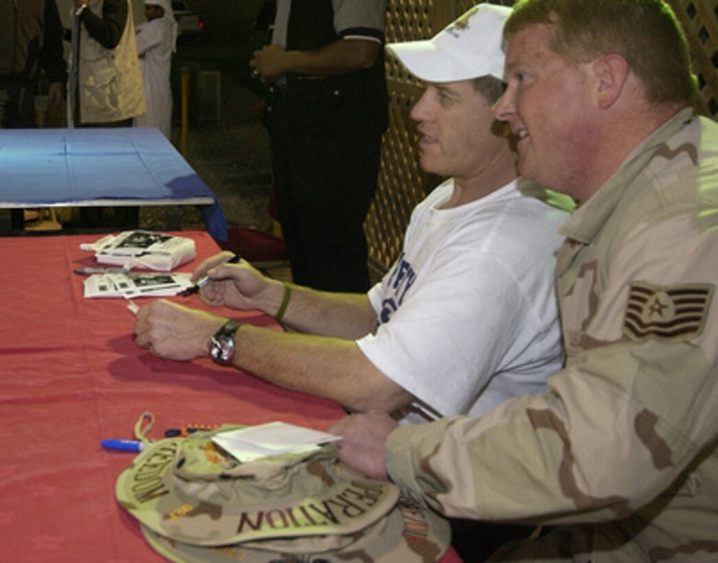 A U.S. Air Force technical sergeant poses for a photo with John Elway as he signs autographs during a United Services Organization show at the 380th Air Expeditionary Wing in Southwest Asia on Dec. 15, 2004. Elway joined Chairman of the Joint Chiefs of Staff Gen. Richard B. Myers, U.S. Air Force, Blake Clark, Leeann Tweeden and Robin Williams on the USO tour to meet, entertain and thank the deployed airmen. 