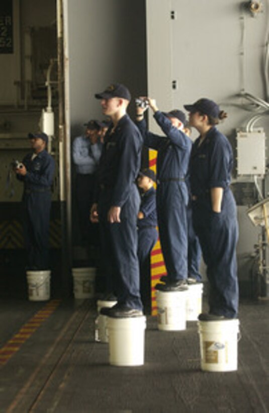 Sailors stand on five gallon buckets so they can see over the crowd during a United Services Organization show aboard the aircraft carrier USS Harry S. Truman (CV 75) anchored near Manama, Bahrain, on Dec. 15, 2004. Chairman of the Joint Chiefs of Staff Gen. Richard B. Myers, U.S. Air Force, Blake Clark, John Elway, Leann Tweeden and Robin Williams on the USO tour to meet, entertain and thank the deployed sailors. 