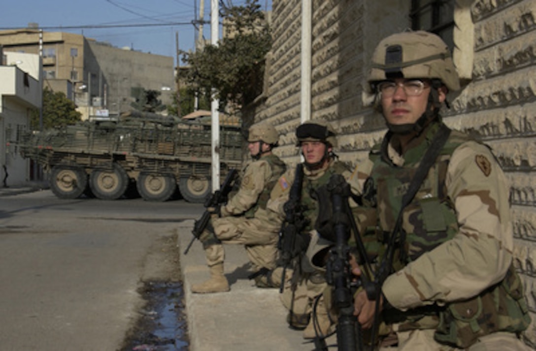 U.S. Army Pfc. William Manley (right), Pvt. Robert Ayres and Spc. Mikhael Medina kneel alongside a building as they provide security for their fellow soldiers during a foot patrol in Mosul, Iraq, on Dec. 10, 2004. The soldiers are assigned to Alpha Company, 1st Battalion, 24th Infantry Regiment, 1st Brigade, 25th Infantry Division Stryker Brigade Combat Team. 