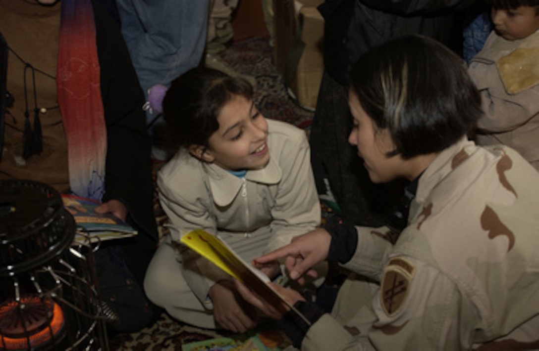 Staff Sgt. Sandy Estrada (right) reads to a girl in a village just outside the town of Qayarah, Iraq, on Dec. 16, 2004. Task Force Olympia and 2nd Battalion, 8th Field Artillery Regiment soldiers visited the area to hand out toys and provide medical treatment. Estrada is assigned to the 426th Civil Affairs Battalion. 