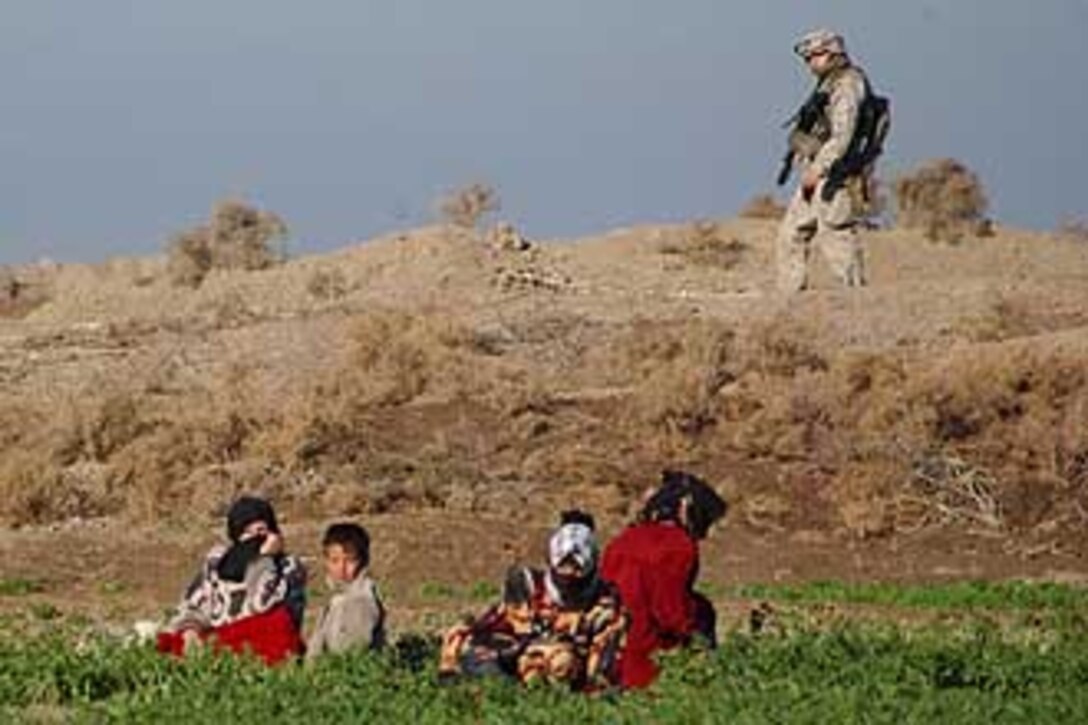 Atop a high, farm field dike, a Marine with 1st Platoon, Company B, 1st Battalion, 23rd Marine Regiment, marches past local Iraqi civilians during a security patrol around Ramadi, Iraq, Dec. 27. In the tradition of their Vietnam predecessors, today?s Marine infantry in Iraq are reinforcing a good relationship between government and local civilians with patrols on the front lines of an insurgency prior to elections January 30.