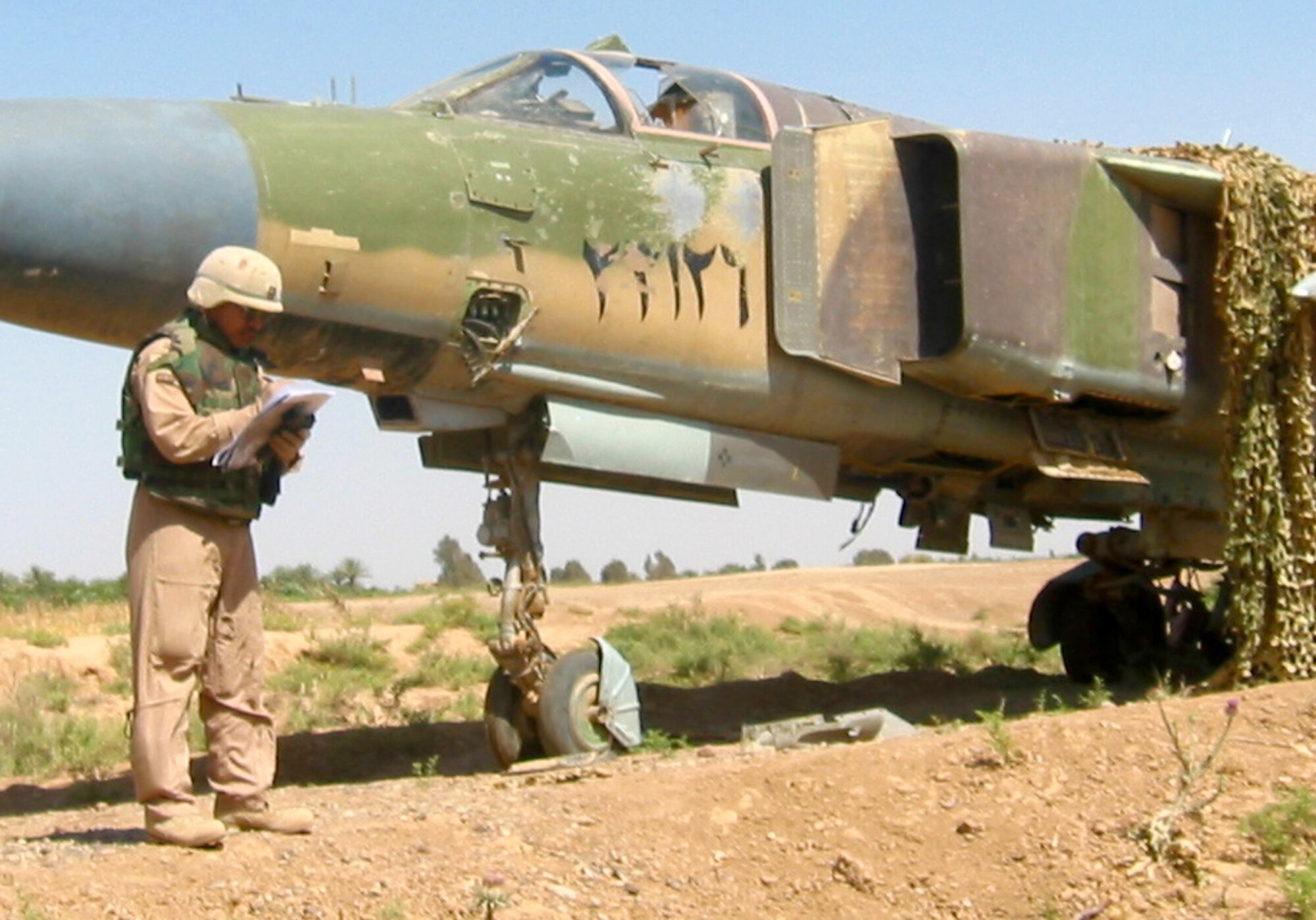 SOUTHWEST ASIA -- Capt. R.C. DeJesus records information about a MiG 23 Flogger found in a field outside Balad Air Base, Iraq.  Captain DeJesus was helping an Army-led effort to move several MiGs back to the base, so that they no longer presented hazards to the local people.  The MiGs were placed throughout the countryside by the Iraqi military before Operation Iraqi Freedom.  Captain DeJesus is an Air Mobility Liaison Officer with the Army's 5th Corps in Heidelberg, Germany.  (Courtesy photo)