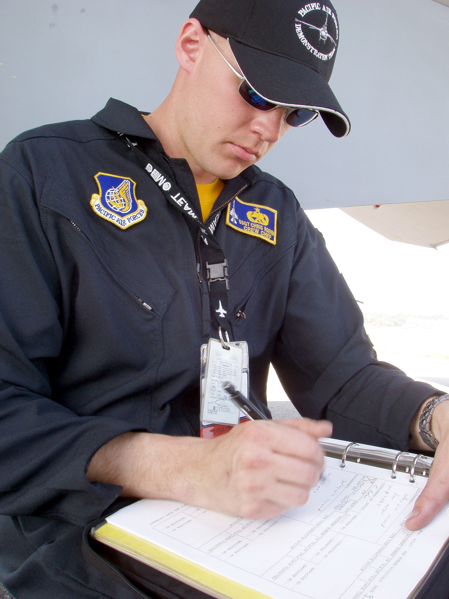 SINGAPORE -- Staff Sgt. Chris Roehm takes a break from the heat in the shadow of an F-16 Fighting Falcon's wing to complete his post-flight paperwork.  Sergeant Roehm, along with the Pacific Air Forces F-16 demonstration team, is here as part of Asian Aerospace 2004, an international air show held every two years.  He is assigned to the 14th Fighter Squadron at Misawa Air Base, Japan.  (U.S. Air Force photo by Capt. Dede Halfhill)