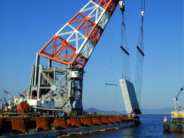 A large cement block is lowered by a large craneas a base for the south side seawall during the construction of the newly finished runway. Construction of the runway was accomplished in three phases. Phase one involved the construction of a new port facility which was completed in 2005. Phase two involved the construction of the north end of the runway while phase three concentrated on the middle.