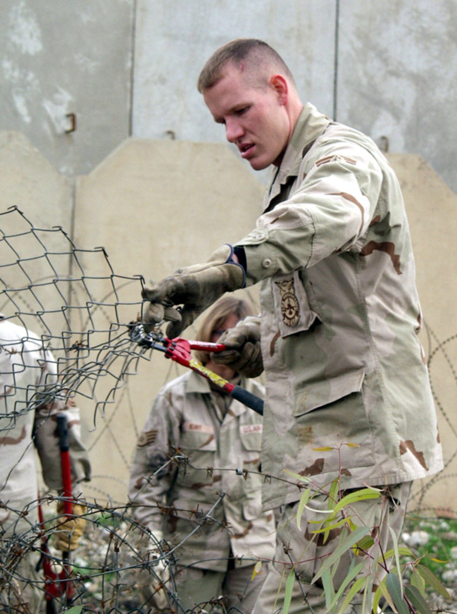 KIRKUK AIR BASE, Iraq -- Staff Sgt. Ryan Darnell cuts through a damaged chain-link fence during the Jan. 11 cleanup effort to help restore a mosque here.  Sergeant Darnell is assigned to the 506th Expeditionary Civil Engineer Squadron here.  (U.S. Air Force photo by Tech. Sgt. Jeffrey Williams)