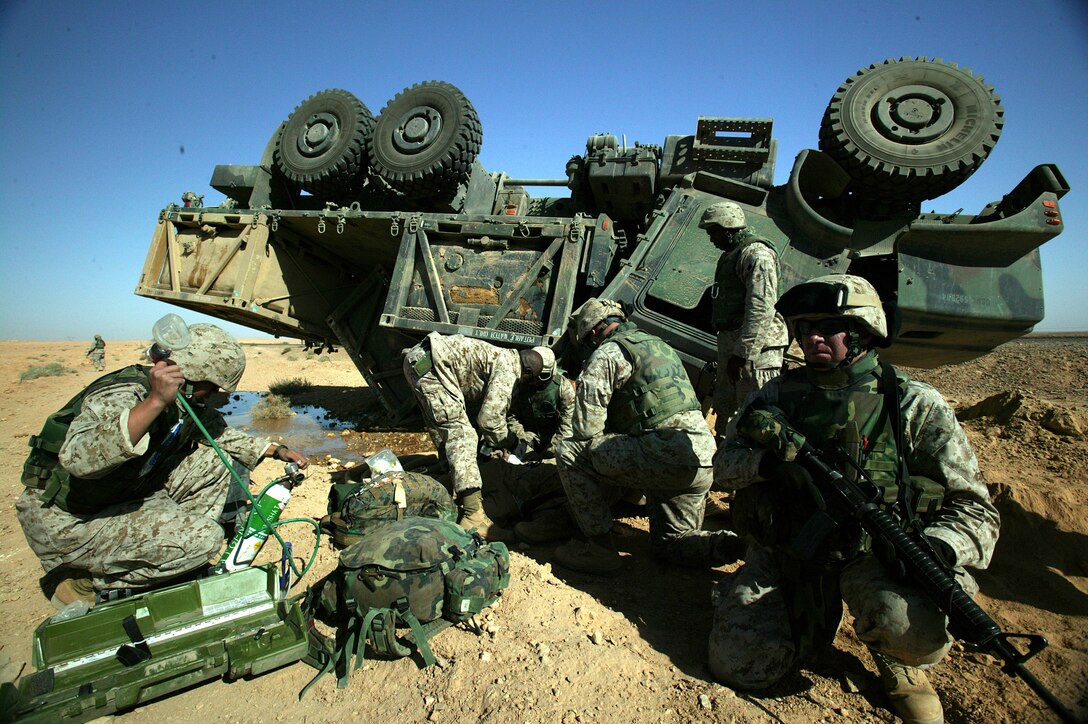 Several Navy corpsmen, Marine, and a Navy Chaplain tend to one of two Marines injured when the seven-ton truck they were driving carrying water overturned during a supply convoy to Camp Korean Village in western Iraq, Oct. 21, 2004. The truck's central tire inflation system malfunctioned, the shift of the thousands of gallons of water it was hauling caused the truck to move off the road and flip over, throwing the Marine manning the machine gun from the turret. Although both Marines involved in the accident suffered only minor injuries, the incident served as a reminder that anything can happen on the open roads of Iraq. The responsibility of delivering everything from food and water to mail and supplemental items, such as magazines and cigarettes, to the remote areas of western Iraq lies in the hands of the Marines of Combat Service Support Company-119. Since August, CSSC-119 Marines have logged in nearly 170,000 miles of road time and put in an average of 90 hours a week. "Marines are going out there and facing the threats that come with convoys - the heat, the distance - it's incredible," said 1st Lt. Chris J. Lefebvre, CSSC-119's executive officer. (Photo by Lance Cpl. T. J. Kaemmerer)