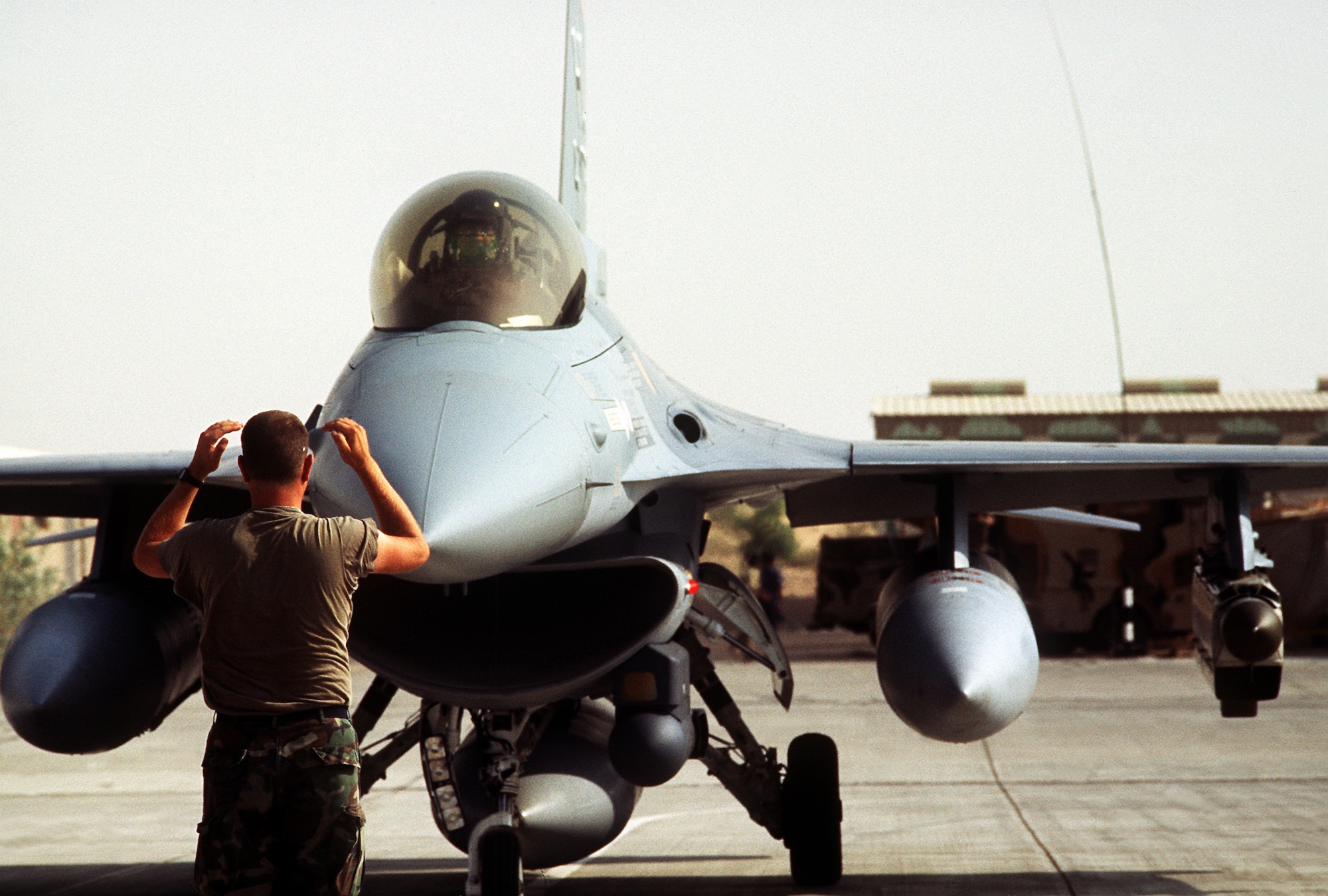 1990's -- A ground crewman guides a 388th Tactical Fighter Wing F-16C Fighting Falcon aircraft onto the taxiway.  The 388th TFW is deploying to Saudi Arabia to take part in Operation Desert Shield.  Mounted on the aircraft's left outboard wing pylon is an AN/ALQ-131 Electronic CounterMeasures pod; mounted on the side of the engine intake is a Low Altitude Navigation, Targeting Infrared Night (LANTIRN) navigation pod.  