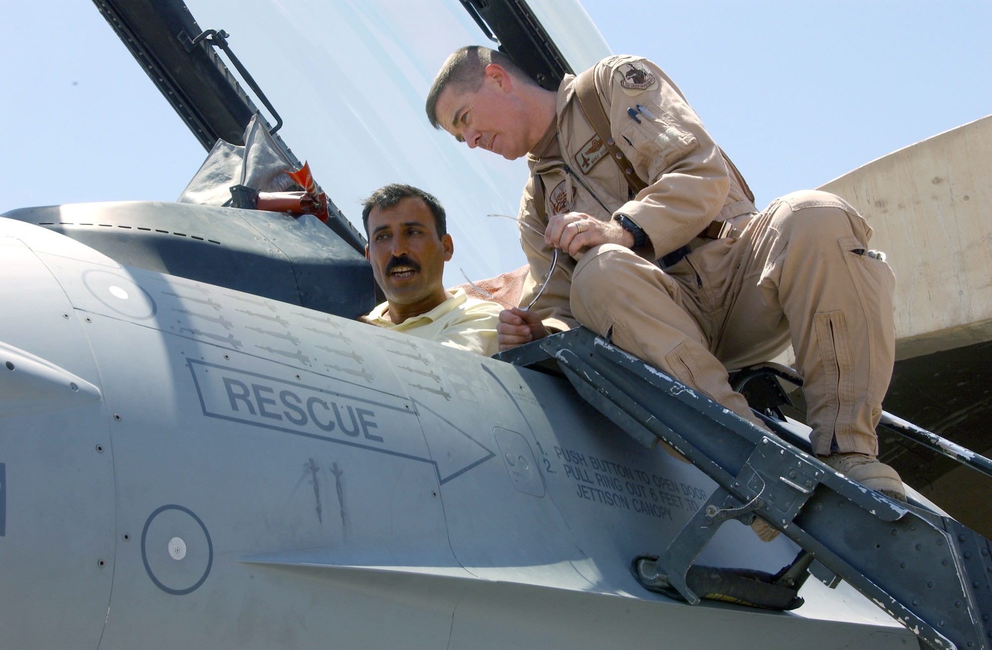 BALAD AIR BASE, Iraq -- Col. Mike Dubie (right) shows an Iraqi fighter pilot the controls of an F-16 Fighting Falcon during a visit here July 20.  Six Iraqi fighter pilots stationed here before Operation Iraqi Freedom had lunch with American pilots and took pictures in front of an aircraft they had flown against for more than a decade.  Colonel Dubie is the 332nd Air Expeditionary Wing director of staff.  (U.S. Air Force photo by Airman 1st Class Heather Norris)