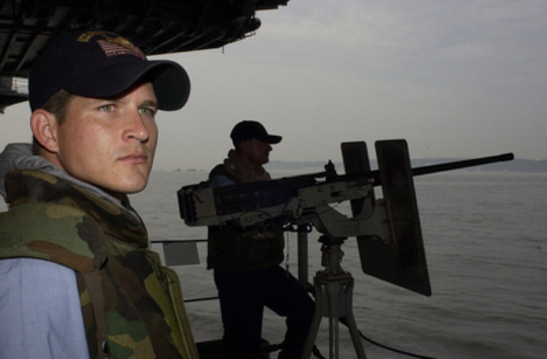 U.S. Navy Airmen Patrick E. Farmer and Luis A. Felix stand a force protection watch at a .50-caliber machine gun onboard the USS Kitty Hawk (CV 63) as the aircraft carrier departs its operating port of Yokosuka, Japan, on July 19, 2004. The Kitty Hawk Strike Group is involved in Summer Pulse '04, a U.S. Naval exercise where seven aircraft carrier strike groups will learn new ways of operating, training, manning and maintaining their fleet. This is part of the Navy's new Fleet Response Plan that will train the fleets to provide assistance in a national emergency or crisis. Farmer and Felix are both assigned to the Kitty Hawk's weapons department. 