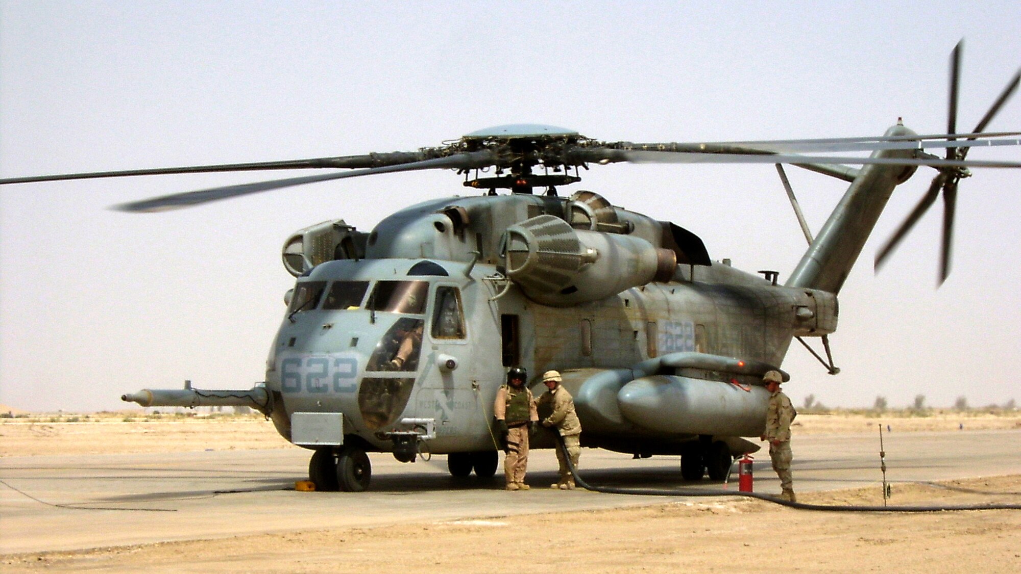 TALLIL AIR BASE, Iraq -- Airman 1st Class Michael Brown (center) refuels a U.S. Marine CH-53E under the watchful eye of and aircrew member as Airman 1st Class Shaun Chadwick(right) stands fire guard.  The helicopter is just one of many aircraft Airmen here service.  They are assigned to the U.S. Army's 439th Petroleum, Oil and Lubricant Forward-Area Refueling Point.  (U.S. Air Force photo by Tech. Sgt. Michael Huntoon)