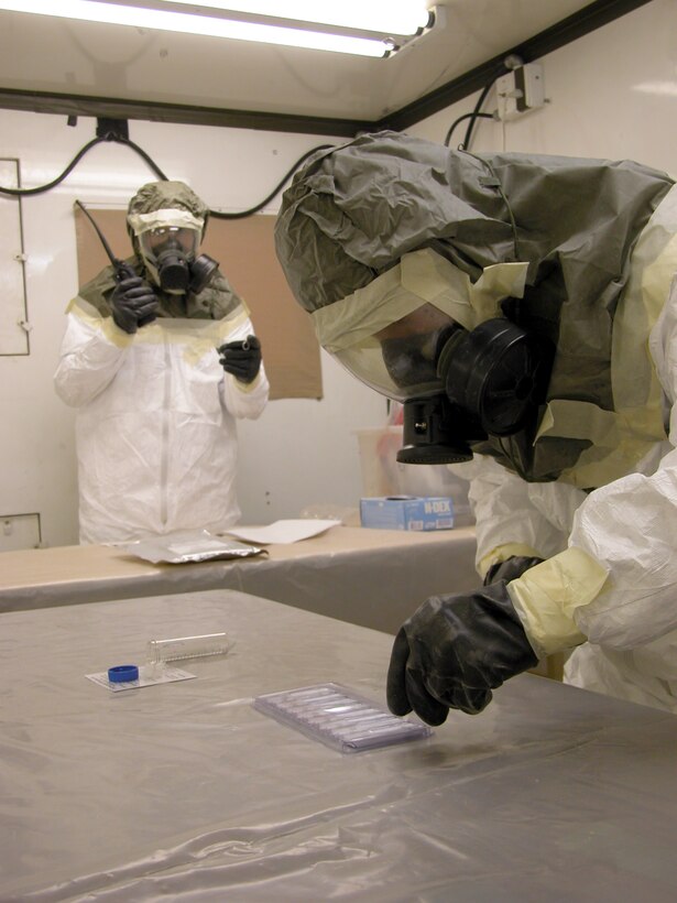 TALLIL AIR BASE, Iraq -- Senior Airman Joshua Burns (right) drops samples of a training agent into a biological-testing kit while Staff Sgt. William Hall uses a stopwatch and notifies the control center of the test start time.  Airman Burns is deployed here from Royal Air Force Lakenheath, England, and Sergeant Hall is from Aviano Air Base, Italy.  Both are readiness journeymen trained to detect nuclear, biological and chemical agents.  (U.S. Air Force photo by Tech. Sgt. Bob Oldham)