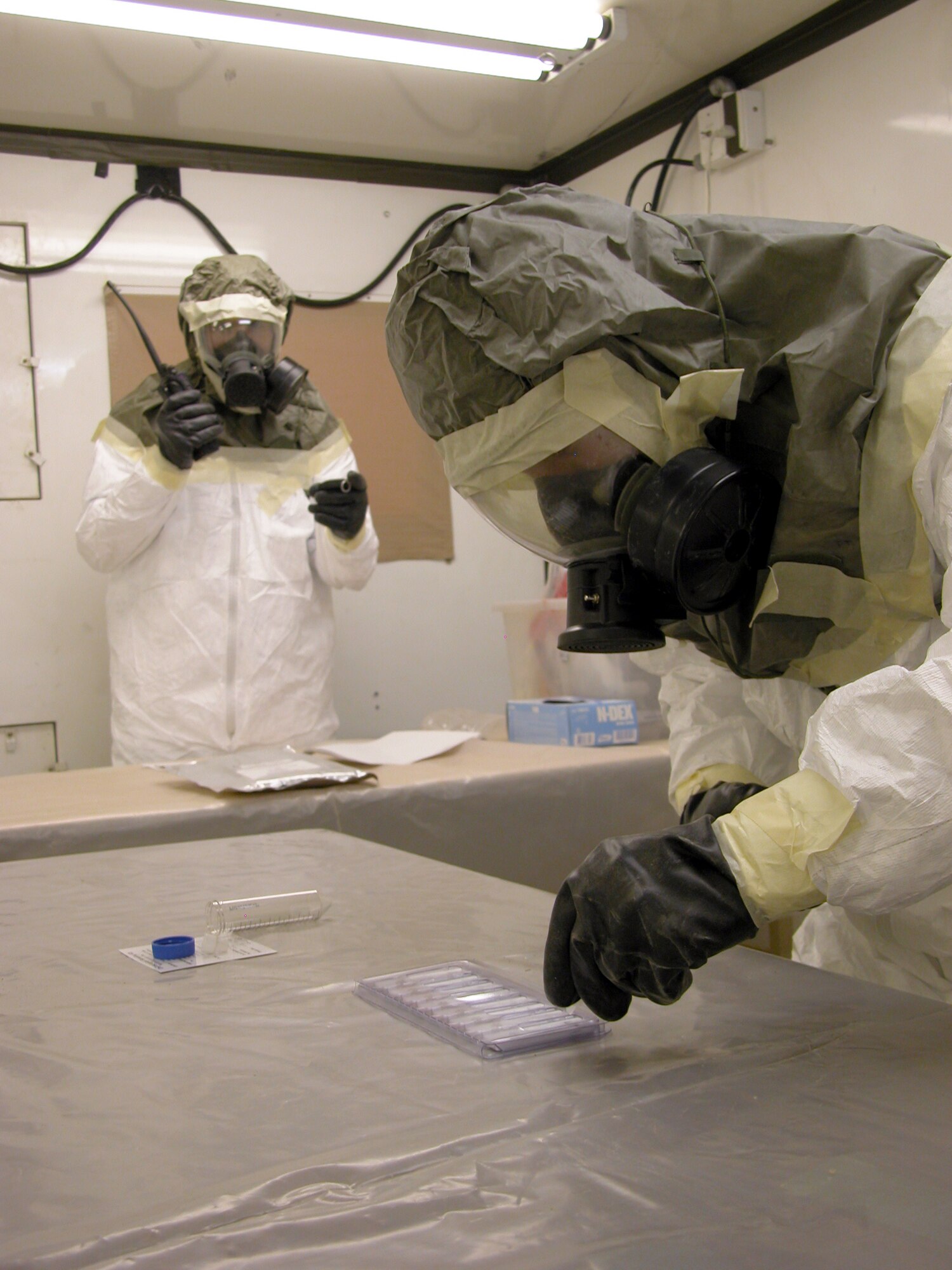TALLIL AIR BASE, Iraq -- Senior Airman Joshua Burns (right) drops samples of a training agent into a biological-testing kit while Staff Sgt. William Hall uses a stopwatch and notifies the control center of the test start time.  Airman Burns is deployed here from Royal Air Force Lakenheath, England, and Sergeant Hall is from Aviano Air Base, Italy.  Both are readiness journeymen trained to detect nuclear, biological and chemical agents.  (U.S. Air Force photo by Tech. Sgt. Bob Oldham)