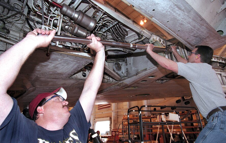 TINKER AIR FORCE BASE, Okla. -- Jerry Byke (left) and Steve LaPlume loosen main landing gear trunnion bolts so the men can inspect for corrosion.  Mr. Byke is a hydraulics aircraft mechanic, and Mr. LaPlume is a flight controls aircraft mechanic.  (U.S. Air Force photo by Margo Wright)