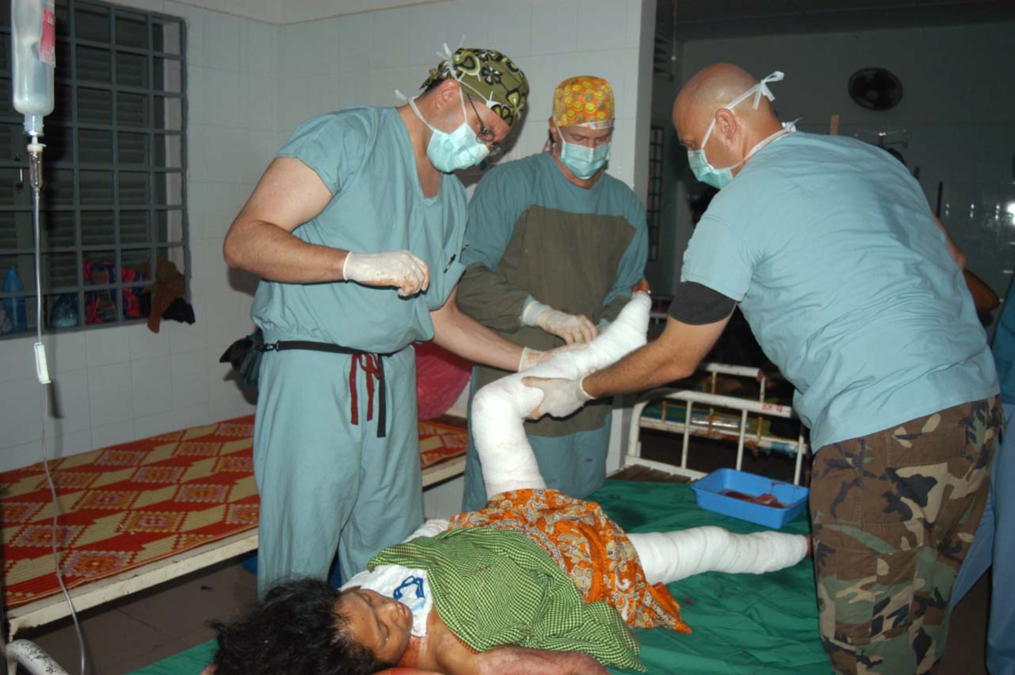 KEP, Cambodia - (From left) Capt. (Dr.) Jason Rosenberg, Lt. Col. (Dr.) Jim Walter and Master Sgt. Kristopher Krenzke bandage a burn patient's legs May 20 at a hospital compound here.  All three Airmen are part of a 20-member blast resuscitation and victim assistance mission.  (U.S. Air Force photo by Master Sgt. Adam Johnston)