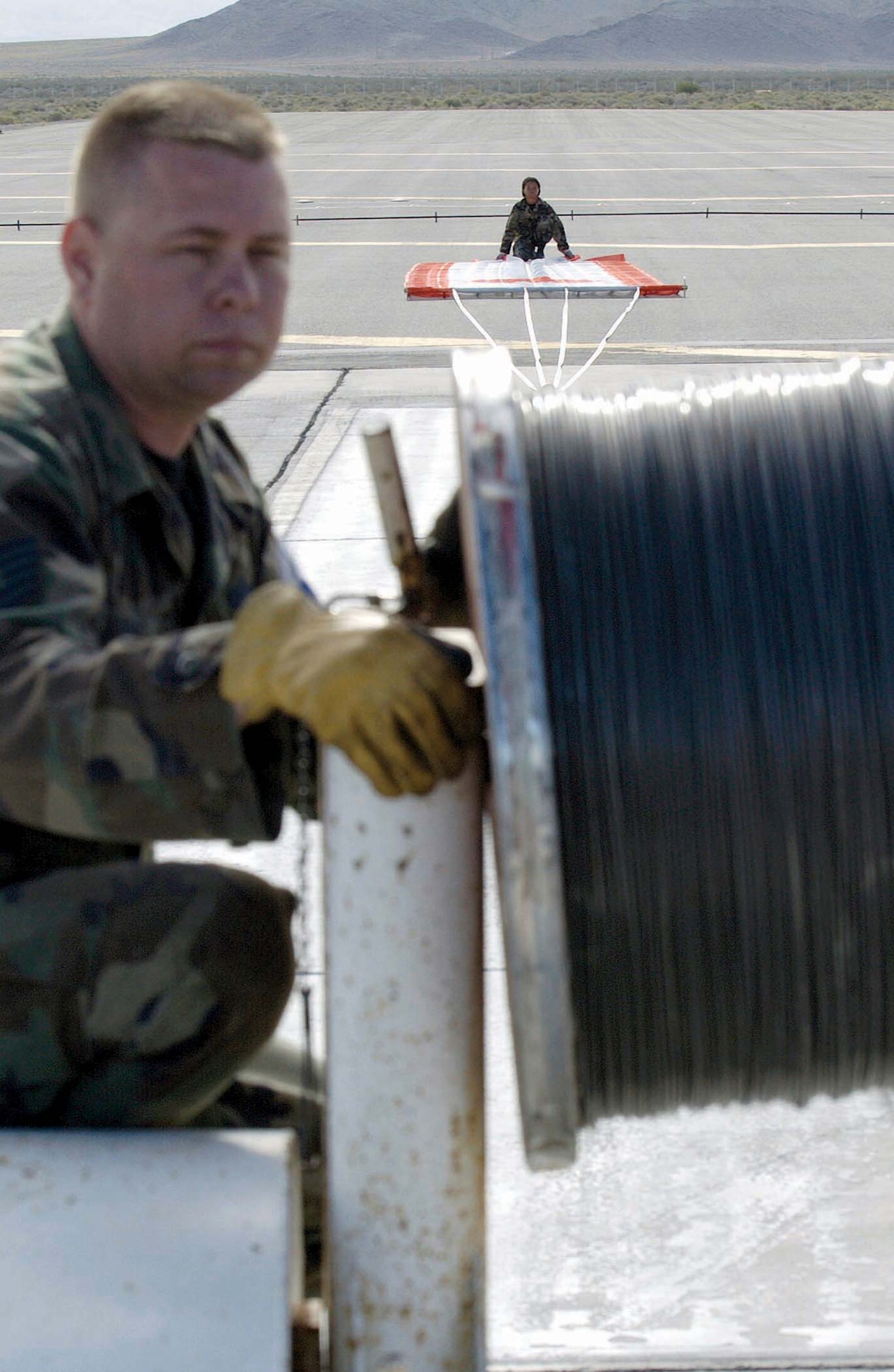 NELLIS AIR FORCE BASE, Nev. -- (From left) Tech. Sgt. Eric Webb extends 1,500 feet of armored cable attached to a banner Senior Airman Edna Burton holds.  The banner was used for target practice by F-15 Eagle pilots during a training exercise May 20 over the Nevada Test and Training Range near here.  Sergeant Webb is assigned to the 390th Fighter Squadron at Mountain Home Air Force Base, Idaho.  Airman Burton is assigned to the 726th Air Control Squadron at Mountain Home AFB.  (U.S. Air Force photo by Senior Airman Brian Ferguson)