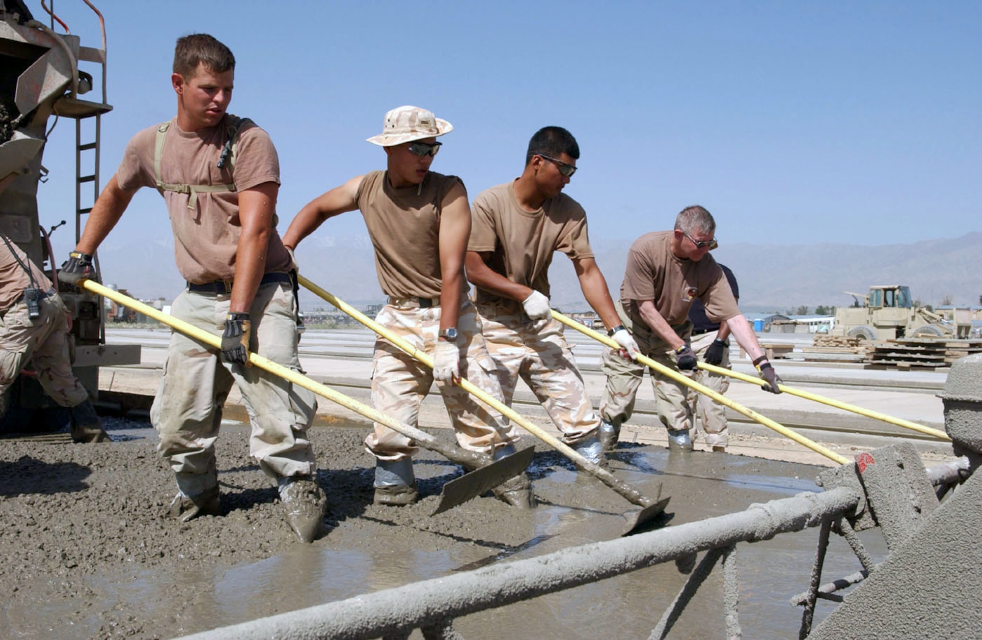 BAGRAM AIR BASE, Afghanistan -- (Left to right) Staff Sgt. Gregory Lund, South Korean army Pfcs. Yi Dong Gon and Jung Yong Hoon, and Col. Gary Woltering work side-by-side "mucking" concrete on the airfield here.  Civil engineers from the 455th Expeditionary Operations Group and the 100th Korean Engineer Corps poured about 76,000 square feet of concrete so aircraft would have more space on the flightline.  Colonel Woltering is the 455th EOG commander.  (U.S. Air Force photo by Master Sgt. Jeff Szczechowski)