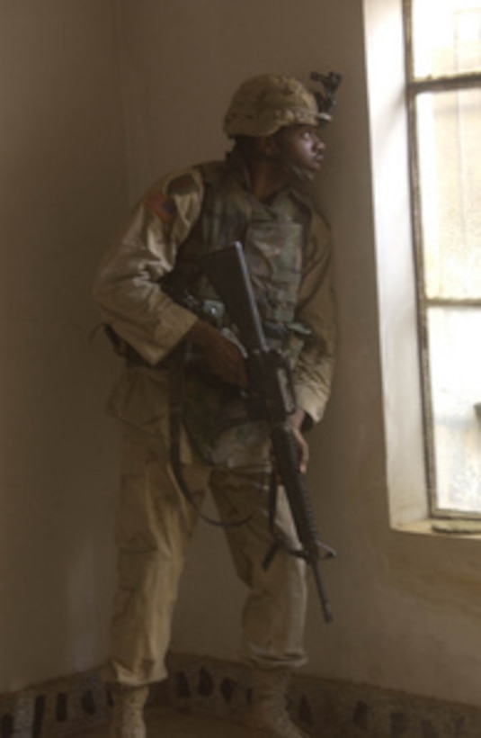 U.S. Army Spc. Deretinald Batiste looks for snipers from inside a house in Fallujah, Iraq, in support of Operation al Fajr (New Dawn) on Nov. 11, 2004. Batiste is assigned as a Signal Support Systems Specialist attached to Alpha Company, Headquarters and Headquarters Company, 2nd Infantry Battalion. 