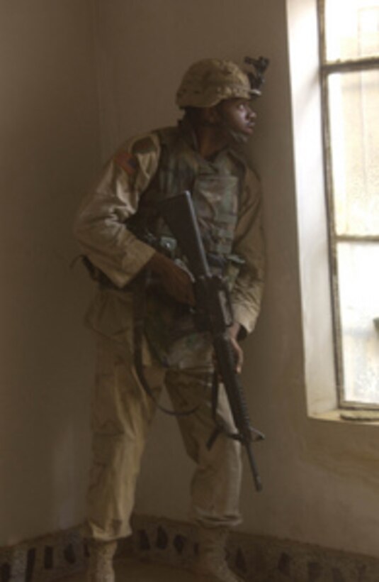 U.S. Army Spc. Deretinald Batiste looks for snipers from inside a house in Fallujah, Iraq, in support of Operation al Fajr (New Dawn) on Nov. 11, 2004. Batiste is assigned as a Signal Support Systems Specialist attached to Alpha Company, Headquarters and Headquarters Company, 2nd Infantry Battalion. 