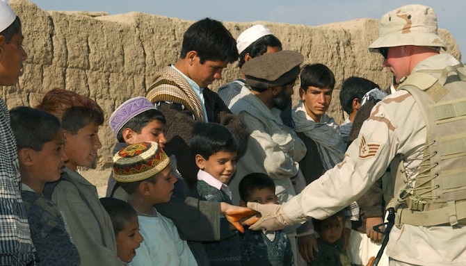 KHAROTI, Afghanistan -- Staff Sgt. James Kamrad shakes hands with young villagers waiting for school supplies to be distributed during a recent adopt-a-village visit.  The 455th Expeditionary Security Forces Squadron force protection intelligence Airman visits local villages often, which he said he enjoys because he gets to learn about local Afghan culture. Sergeant Kamrad is deployed to nearby Bagram Air Base from Pope Air Force Base, N.C., supporting Operation Enduring Freedom  (U.S. Air Force photo by Staff Sgt. Jennifer Lindsey)