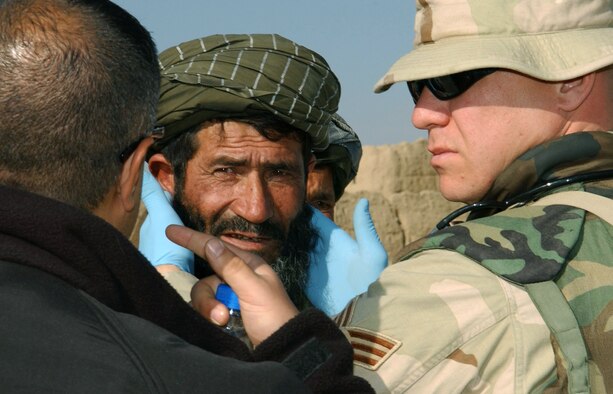 KHAROTI, Afghanistan -- Senior Airman Jason Weiss lightly rubs behind a villager's ears to see if the man experiences discomfort, which is one of the common symptoms of a sinus infection.  Through an interpreter, the Afghan shared complaints of facial pain, a stuffy nose and sore throat with Airman Weiss who treated him with medication.  In about three hours, the medical technician evaluated and provided minimal treatment for about 60 patients.  He is deployed to nearby Bagram Air Base from Spangdahlem Air Base, Germany supporting Operation Enduring Freedom.  (U.S. Air Force photo by Staff Sgt. Jennifer Lindsey)