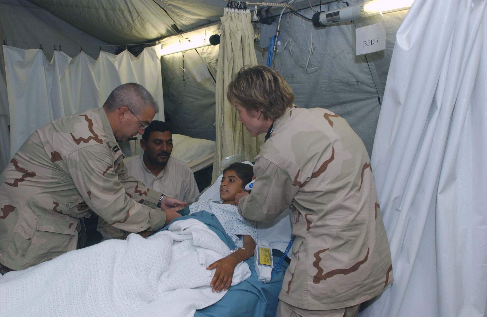 TALLIL AIR BASE, Iraq -- Capts. Robert Hayes and Jeannette Ward monitor 8-year-old Nahida under the watchful eyes of her father, Nafl Radi.  The young Iraqi girl was bitten by a venomous snake and treated at the medical facilities here.  The Airmen are nurses with the 407th Expeditionary Medical Group.  (U.S. Air Force photo by Staff Sgt. Maria Bare)