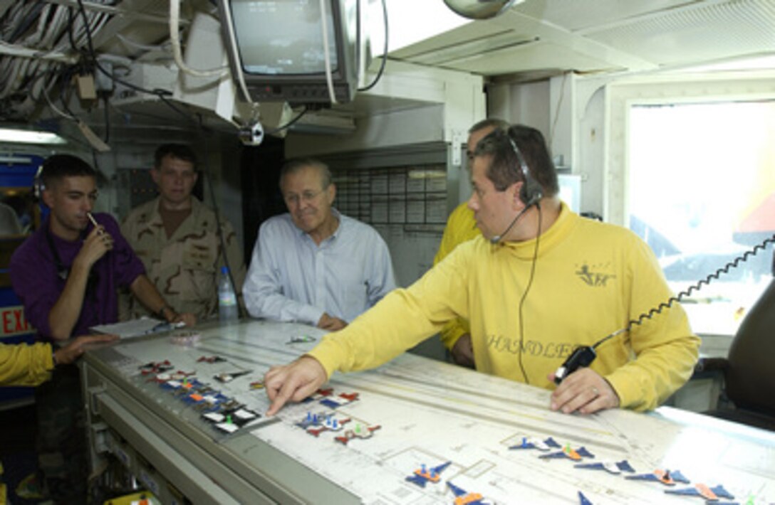 Lt. Cmdr. Daryl Wall shows Secretary of Defense Donald H. Rumsfeld (center) a graphic representation of the flight deck onboard the USS John F. Kennedy (CV 67) on Oct. 9, 2004. More commonly known as the "Ouija Board," it allows the aircraft handlers to forecast aircraft position on the flight deck. Rumsfeld is onboard the aircraft carrier to meet with crewmembers and host coalition ministers of defense. 