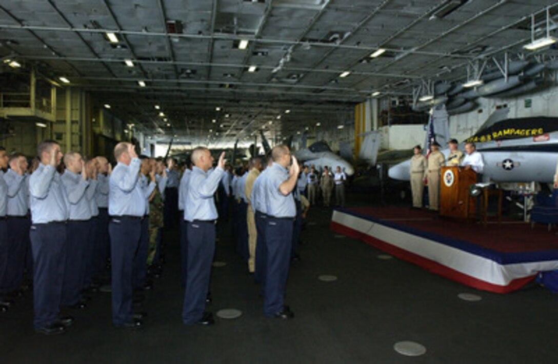Secretary of Defense Donald H. Rumsfeld reads the oath of enlistment to eighty-five service members during a reenlistment ceremony aboard the USS John F. Kennedy (CV 67) on Oct 9, 2004. Rumsfeld is onboard the aircraft carrier to meet with crewmembers and host coalition ministers of defense. 