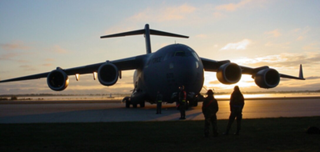 A U.S. Air Force C-17 Globemaster III and its maintenance personnel are silhouetted by the morning sun as they prepare for a morning mission at Phelps-Collins Air National Guard Base in Alpena, Mich., on Oct. 21, 2004. 