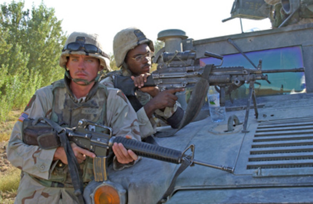 Pvt. William Knight (left) and Pfc. Gregory Guyton keep a sharp watch for suspicious activity as other 1st Infantry Division soldiers and members of the Iraqi National Guard sweep for improvised explosive devices during a joint day patrol outside the city of Baqubah, Iraq, on Aug. 23, 2004. 