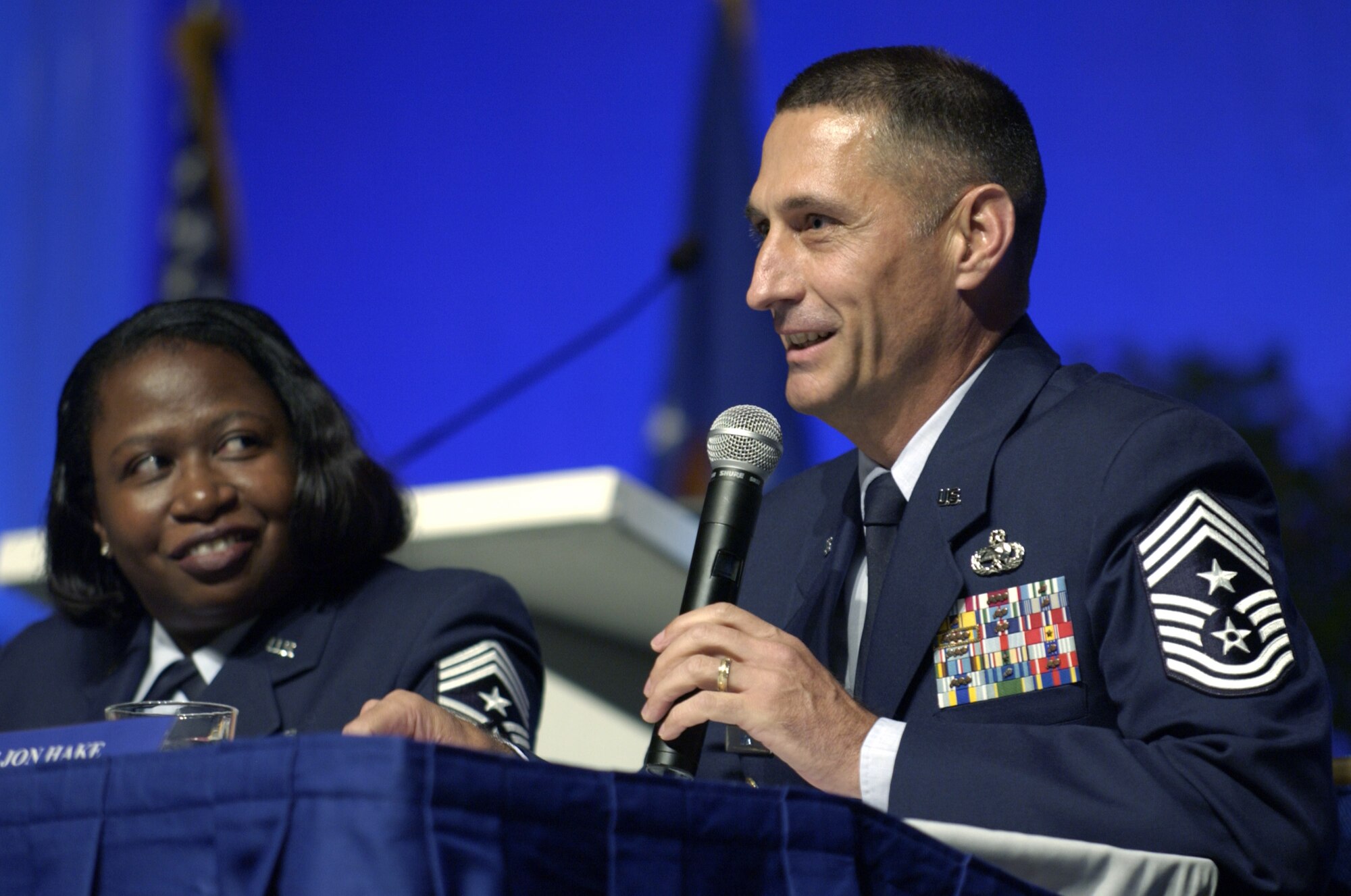 WASHINGTON -- Chief Master Sgt. Cheryl Adams (left) listens as Chief Master Sgt. Jonathan Hake speaks to the crowd during a forum at the Air Force Association's 2004 Air and Space Conference and Technology Exposition here Sept. 13.  Chief Adams is command chief for Air Force Reserve Command, and Chief Hake is command chief for Air Force Materiel Command.  (U.S. Air Force photo by Master Sgt. Jim Varhegyi)