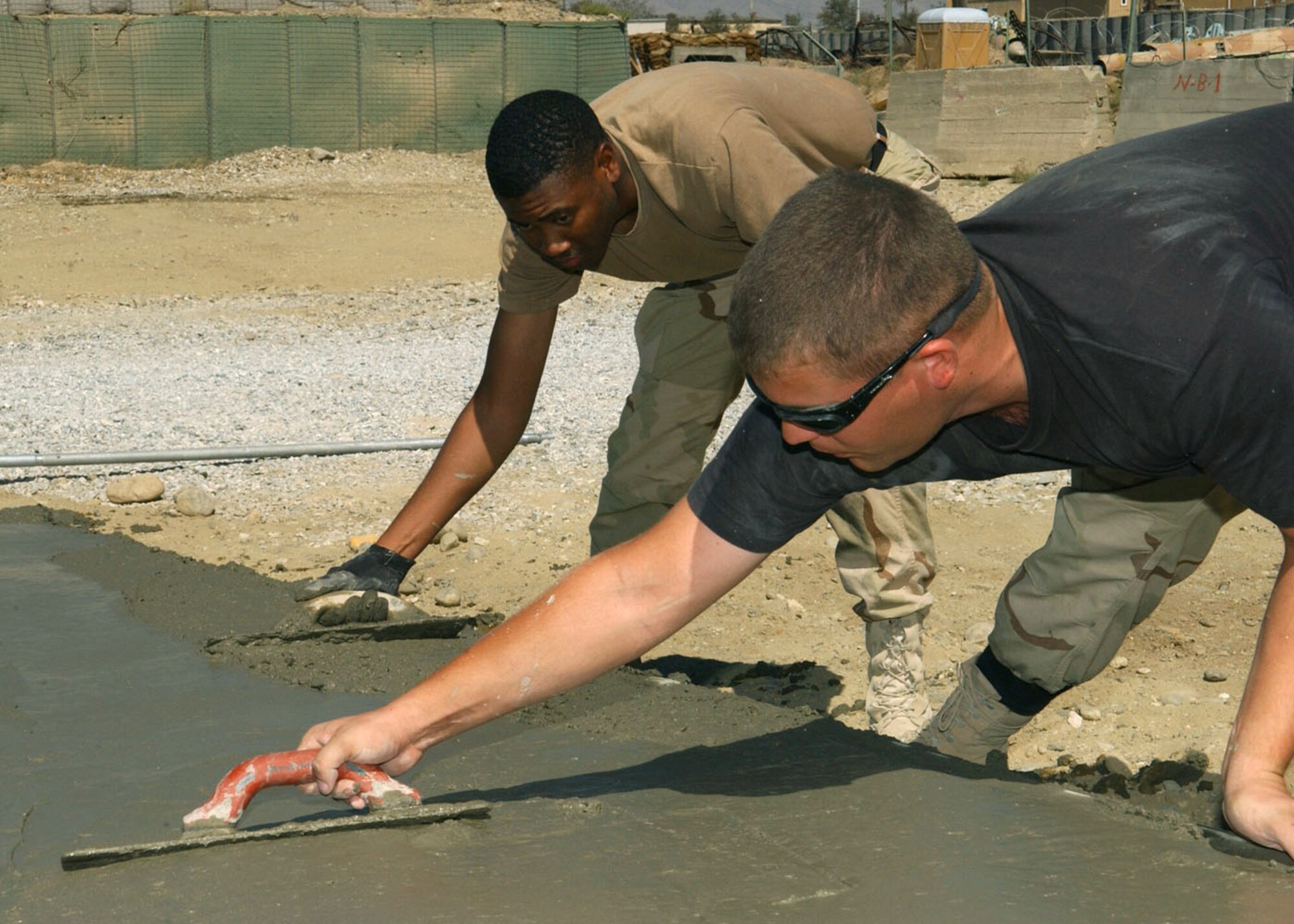 BAGRAM AIR BASE, Afghanistan -- Airman 1st Class David Depouw (foreground) and Senior Airman Derland Ellison ensure a newly poured pad will have a smooth finish by using magnesium floats to get the rocks down before the concrete dries.  Airman Depouw and Sergeant Ellison are assigned to the 455th Expeditionary Operations Group's civil engineer flight here as a heavy-equipment apprentice and journeyman, respectively.  (U.S. Air Force photo by Staff Sgt. Jennifer Lindsey)