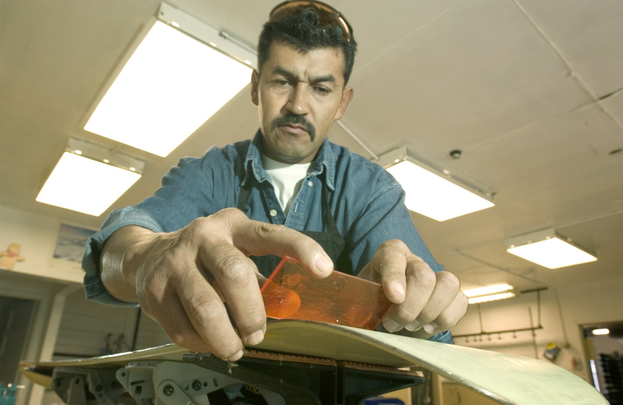 MOUNTAIN HOME AIR FORCE BASE, Idaho -- Raul Hernandez uses a plastic scraper to shave excess wax off a snowboard he is refurbishing at the base outdoor recreation supply office.  The base's only certified ski-equipment maintainer cares for more than 600 pairs of skis, 100 snowboards and countless cross-country skis, snowshoes and sleds.  (U.S. Air Force photo by Master Sgt. Lance Cheung)