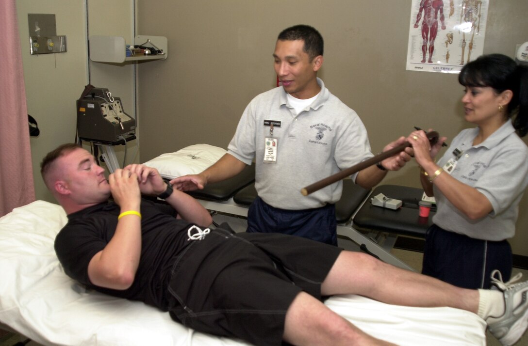 MARINE CORPS BASE CAMP LEJEUNE, N.C. - Physical therapist technicians Petty Officer 2nd Class Francis Rosanes and Romona Walters explain a wand excerise to Sgt. Homer Miller, a field radio operator from the 24th Marine Expeditionary Unit. Miller, who is rehabbing an over-use injury to his left shoulder, is scheduled to have surgery on both his ankle and knee later in the year. "I never want to get hurt," said Miller. "But they do a wonderful job here, outstanding work actually." (Official Marine Corps photo by Lance Cpl. Shane Suzuki)