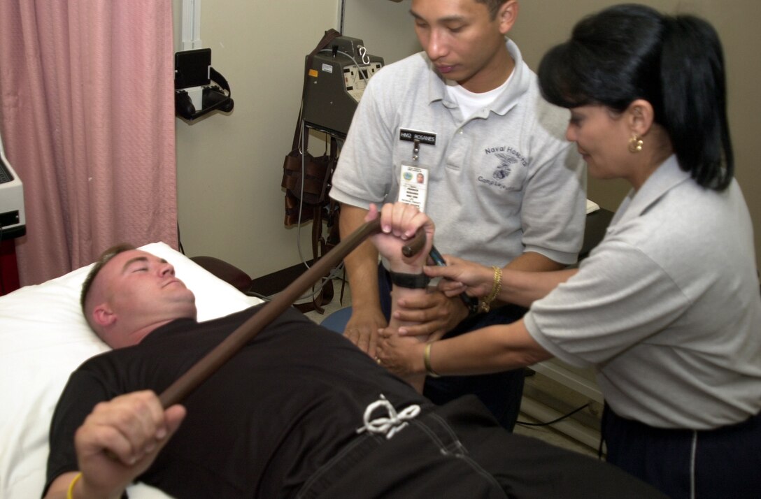 MARINE CORPS BASE CAMP LEJEUNE, N.C. - Physical therapist technicians Petty Officer 2nd Class Francis Rosanes and Romona Walters explain a wand excerise to Sgt. Homer Miller, a field radio operator from the 24th Marine Expeditionary Unit. Miller, who is rehabbing an over-use injury to his left shoulder, is scheduled to have surgery on both his ankle and knee later in the year. "I never want to get hurt," said Miller. "But they do a wonderful job here, outstanding work actually." (Official Marine Corps photo by Lance Cpl. Shane Suzuki)