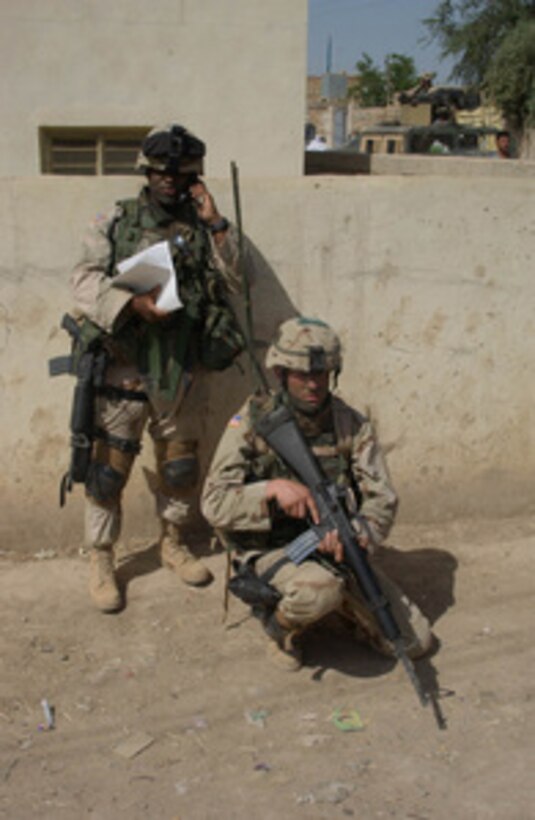 One soldier from Bravo Company, 130th Infantry Battalion, kneels down as he provides security for another talking on the radio during a search for weapons and possible insurgents in Baqubah, Iraq, on April 12, 2005. These soldiers are attached the 3rd Brigade Combat Team. 