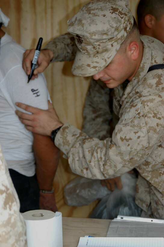 CAMP HURRICANE POINT, Ar Ramadi, Iraq (April 29, 2005) -Corporal Dan L. Grabinski, legal administrative clerk with Headquarters and Service Company, 1st Battalion 5th Marine Regiment, uses a permanent marker to write information on a suspect insurgent as he fills his secondary billet as the day non commissioned officer in-charge of the detainee facility here. The 21-year-old from Schiller Park, Ill., processes expected insurgents his fellow infantry battalion leathernecks snatched up out of the city while conducting security and stabilization missions. With help from three other Marines, Grabinski runs the detainees through the biometric automative tools system, which helps them distinguish members of the insurgency from innocent Iraqi civilians. Detainees found guilty of committing terrorist acts are sent to the Abu Ghraib Prison. Photo by Cpl. Tom Sloan