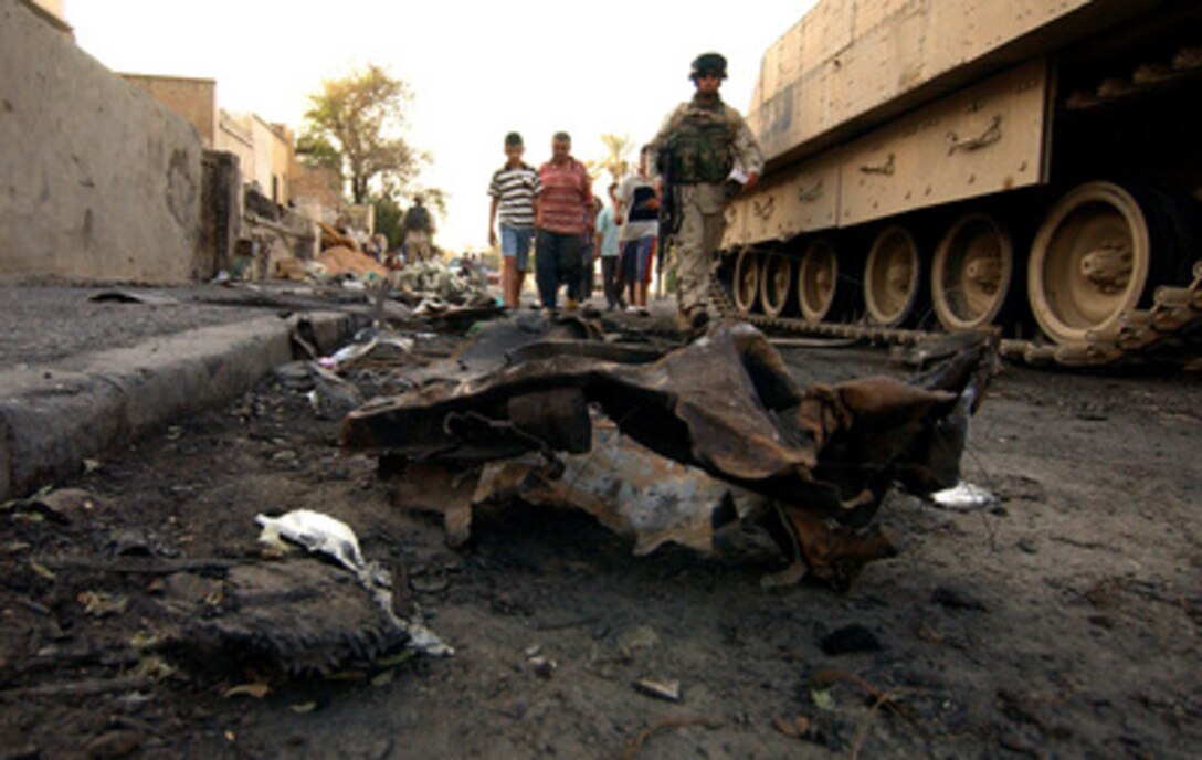 U.S. Army soldiers from Delta Company, 164th Armor Regiment secure a street known as Route Predators while Iraqi civilians collect materials to fix their homes and businesses in Baghdad, Iraq, on July 27, 2005. The structures were damaged after a vehicle born improvised explosive device detonated near a clinic targeting innocent civilians in Baghdad. 