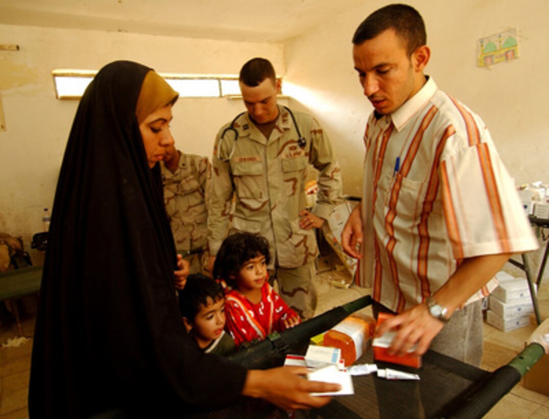 Iraqi Dr. David Salman (right) discusses medications with an Iraqi woman during a Medical Civil Action Program at Fenjan Village near Baghdad, Iraq, on July 26, 2005. Salman is working with U.S. Army Capt. Jeremy Edwards (center) from the 3rd Squadron, 7th Cavalry Regiment, whose medical staff provides periodic health care and assistance to civilians in different locations. 