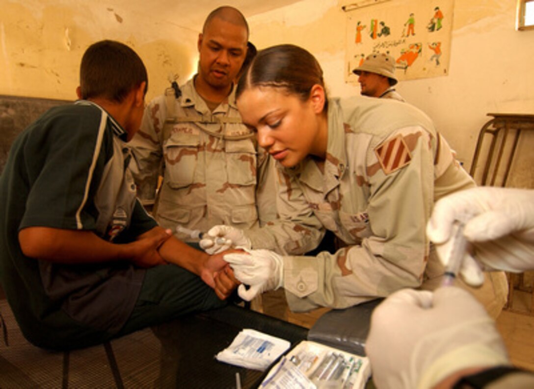 U.S. Army Pfc. Maya Madlock inserts a needle into the infected area of an Iraqi boy's thumb during a Medical Civil Action Program at Fenjan Village near Baghdad, Iraq, on July 26, 2005. Madlock is assigned to the 3rd Squadron, 7th Cavalry Regiment, whose medical staff provides periodic health care and assistance to civilians in different locations. 