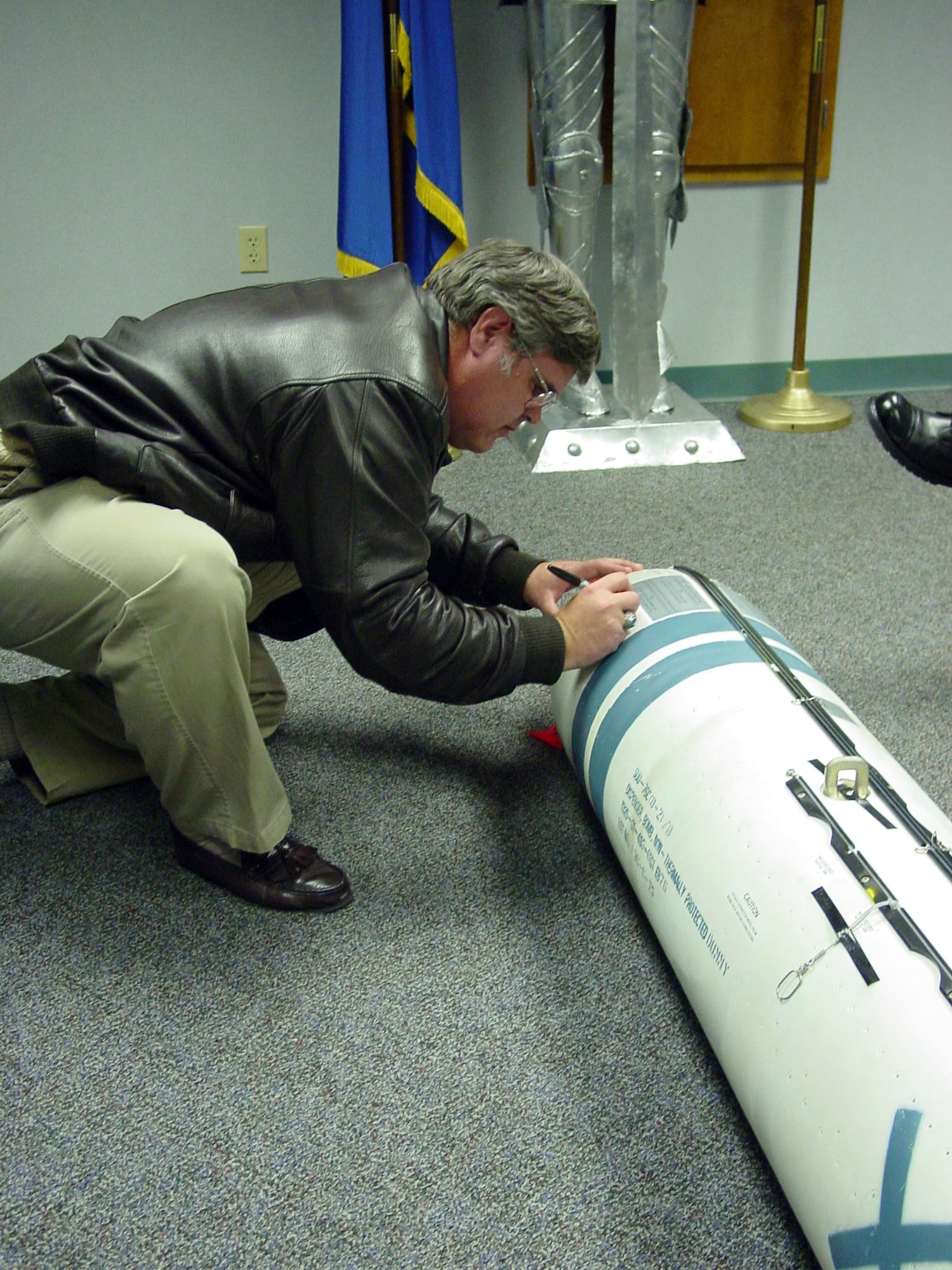 LACKLAND AIR FORCE BASE, Texas - Retired Master Sgt. Chuck Doig, formerly of the Air Intelligence Agency psychological operations division, signs a display model of the PDU-5/B leaflet bomb. Sergeant Doig submitted an idea to the Air Force Information Warfare Battlelab to convert a Rockeye cluster bomb canister into a new leaflet delivery system. (U.S. Air Force photo by Staff Sgt. Ted Guerrero)