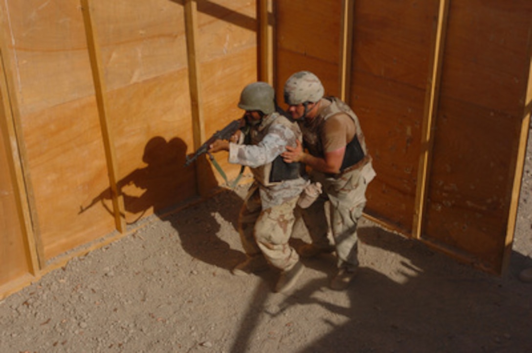 A U.S. Army soldier guides an 8th Division Iraqi Army soldier as he participates in a Shoot House live fire weapons training exercise at the Iraqi Army Compound on Forward Operating Base Iskandariyah, Iraq, on July 30, 2005. Members of the U.S. Army Multinational Training Team, part of the 155th Brigade Combat Team, are training Iraqi Army soldiers to increase their proficiency. 