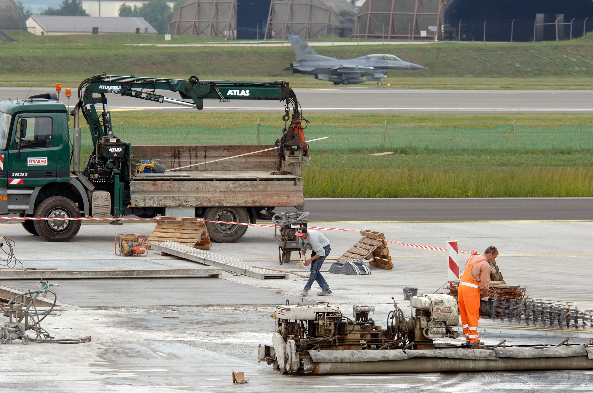 SPANGDAHLEM AIR BASE, Germany -- Construction workers continue to finish the Air Mobility Command parking ramp here as an F-16 Fighting Falcon lands after a training sortie.  The multimillion-dollar construction project is part of the Rhein-Main Transition Program.  By Oct. 1, the 726th Air Mobility Squadron will set up operations at this fighter base.  (U.S. Air Force photo by Senior Master Sgt. Keith Reed)