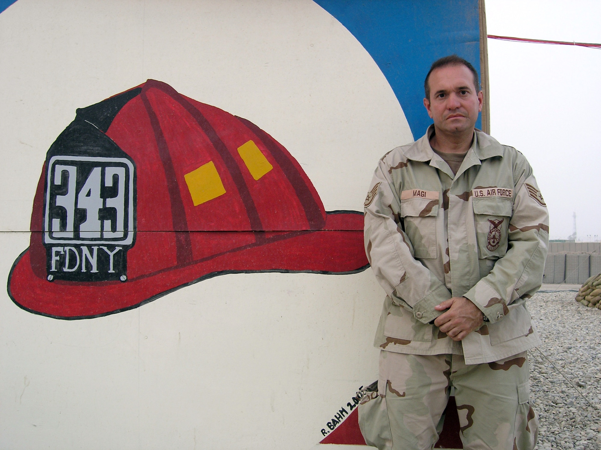 ALI BASE, Iraq -- Staff Sgt. Gregg Magi poses in front of a mural remembering the 343 firefighters who lost their lives at Ground Zero trying to help the victims of Sept. 11, 2001.  Sergeant Magi was promoted to the rank of lieutenant in the Fire Department City of New York during a ceremony via telephone Aug. 16.  He is a firefighter with the 407th Expeditionary Civil Engineer Squadron and is deployed from the New York Air National Guard's 105th Airlift Wing.  (U.S. Air Force photo by Tech. Sgt. Melissa Phillips)