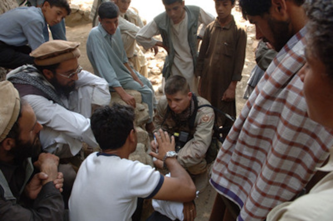 Afghani men and boys surround Army Sgt. Matthew MacRoberts as he interviews the local mullah in the village of Qual-A-Atakhom, Afghanistan, on Aug. 16, 2005. MacRoberts, of Task Force Eagle, is visiting the village as part of a Medical Civil Action Program. 