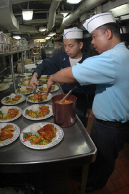 Petty Officer 1st Class Rogelio Magpantay (right) and Petty Officer 2nd Class Gomer Cubol prepare entrees for a ward room dinner on board the aircraft carrier USS Kitty Hawk (CV 63) on July 19, 2005. The Culinary Specialists of the Kitty Hawk supply department serve 17,000 daily meals to a crew of 5,300. 